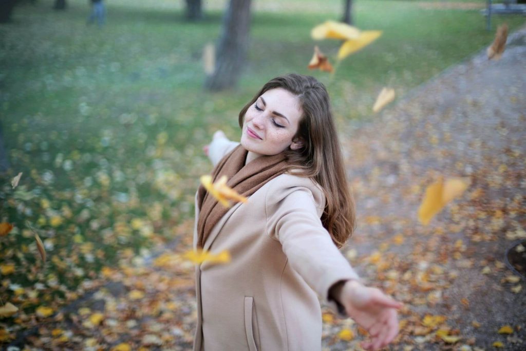 Woman with arms wide open, smiling, with autumn leaves falling
